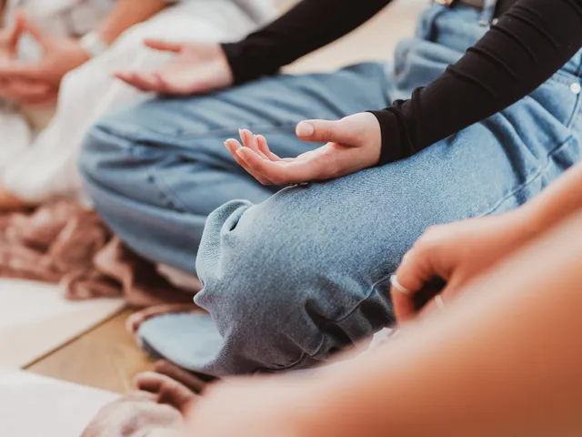 Close-up of hands resting open on crossed knees as a group sits in meditation at Davaar House